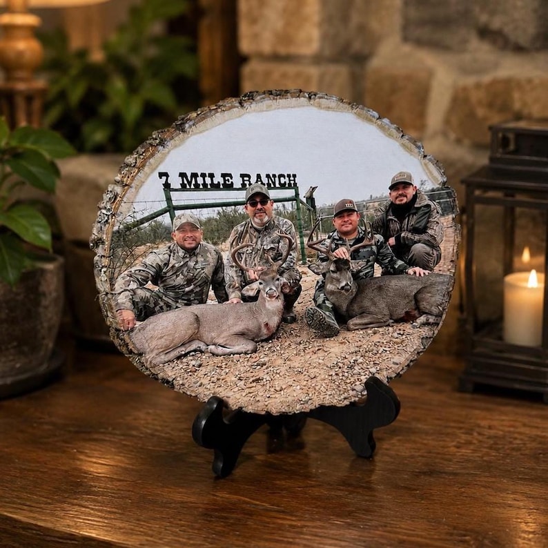 May include: A circular wood slice plaque featuring a printed photograph of four people in camouflage clothing posing with two deer in front of a sign that reads 7 MILE RANCH. The plaque has a natural bark edge and rests on a black plastic display stand.