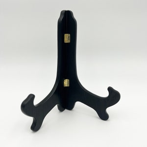 May include: Black wooden easel stand with gold hinges. The stand is folded and has a triangular shape.