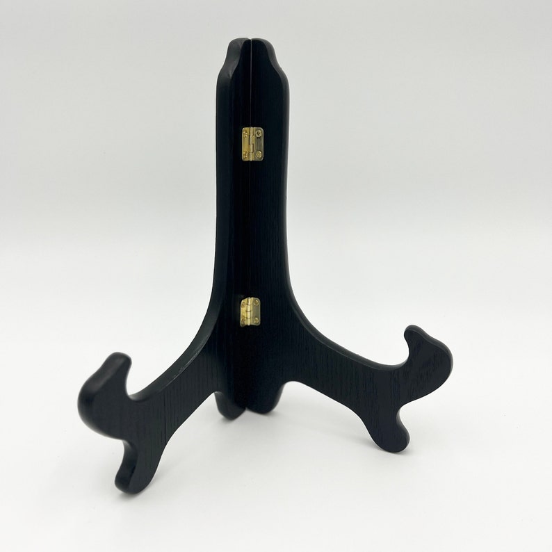 May include: Black wooden easel stand with gold hinges. The stand is folded and has a triangular shape.