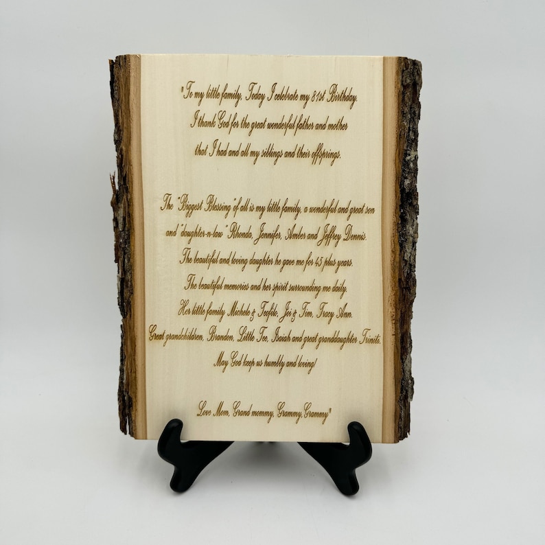 May include: A rectangular light-colored wooden plaque with natural bark edges on the left and right sides. The plaque is supported by a black plastic stand and features dark laser-engraved text detailing a family message for an 81st birthday.