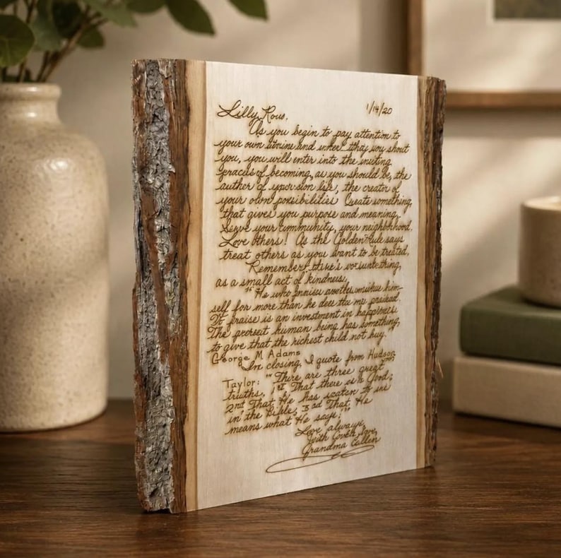 May include: A rectangular wooden plaque with natural bark edges on the sides. The light-colored wood surface features dark, laser-engraved cursive text that reads as a letter dated 1/14/20, signed by Grandma Callen, and includes a quote by George M. Adams.