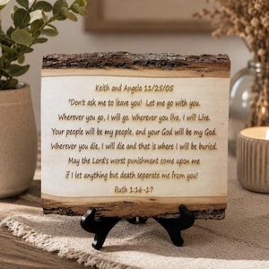 May include: A rectangular wooden plaque with natural bark edges, displayed on a black stand. The light-colored wood surface features laser-engraved text: Keith and Angela 11/25/05, followed by the biblical passage Ruth 1:16-17 in dark brown lettering.