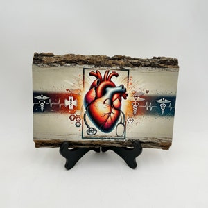 Puede incluir: Una placa de madera con una ilustraci&oacute;n anat&oacute;mica de un coraz&oacute;n rojo, rodeada de s&iacute;mbolos m&eacute;dicos y un estetoscopio. El fondo es una veta de madera clara con un degradado azul y rojo.