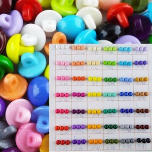 May include: A colour chart of small round plastic buttons with a variety of colours. The chart is labelled with numbers and letters. The buttons are arranged in rows and columns.