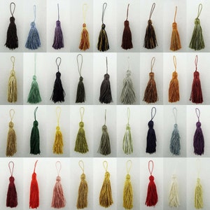 May include: A collection of tassels in a variety of colours, such as black, blue, purple, gold, brown, green, and red. Each tassel has a loop for hanging. The tassels are made of a soft, textured material.