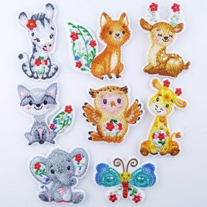 May include: Set of 8 embroidered iron-on patches featuring various animals and a butterfly. The animals include a zebra, fox, deer, raccoon, owl, giraffe, elephant, and a butterfly. The patches are all white with colourful embroidery.