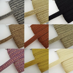 May include: Nine spools of decorative trim in various colours, including black, gold, brown, and purple. The trim features intricate woven patterns and textures, suitable for crafts and embellishments.