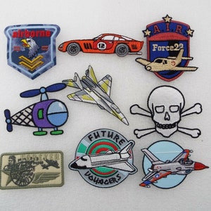 May include: A selection of embroidered patches with diverse designs. Includes a red race car, a skull and crossbones, a helicopter, a jet, a space shuttle with "Future Voyagers" text, and military-themed patches with eagles and text.