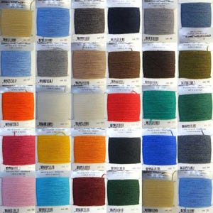 May include: A collection of 24 yarn samples in various colours, including beige, blue, grey, brown, orange, red, green, black, and white. Each sample is labelled with a colour number and the word "SCANFIL".