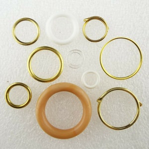 May include: Assortment of different sized rings in gold, white, and beige. The rings are made of metal, plastic, and glass.