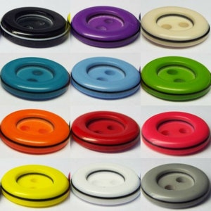 May include: Assortment of 12 two-hole plastic buttons in various colours, including black, purple, cream, teal, light blue, green, orange, red, pink, yellow, white, and grey. Each button has a black rim.