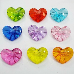 May include: Assortment of ten heart-shaped buttons in various colors, including green, red, blue, purple, pink, yellow, and orange. The buttons are made of clear plastic and have a raised design.