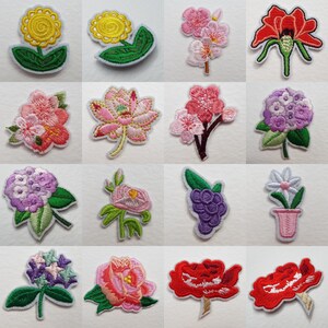 May include: A selection of embroidered floral patches in various colours. The patches include a yellow sunflower, pink cherry blossoms, a red poppy, a purple hydrangea, and a pink lotus flower. Each patch has a white border.