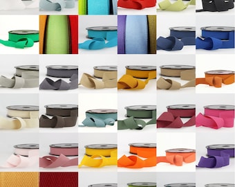May include: A collection of 36 spools of cotton webbing in various colors, including white, black, red, green, blue, yellow, orange, and brown. The spools are arranged in a grid pattern on a white background.