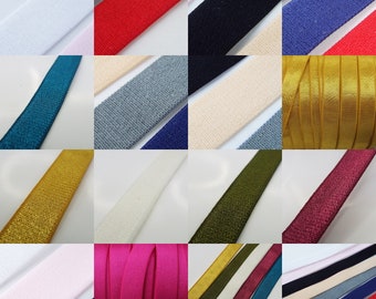 Könnte beinhalten: Sortiment aus elastischem Band in verschiedenen Farben und Texturen, darunter einfarbig, Glitzer und Satin. Das Band ist in einem Rastermuster auf weißem Hintergrund angeordnet.