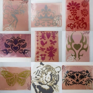May include: Nine different stencils on pink and white backgrounds. The stencils feature a variety of designs, including a crown, a butterfly, a heart, a tiger, and a floral pattern.