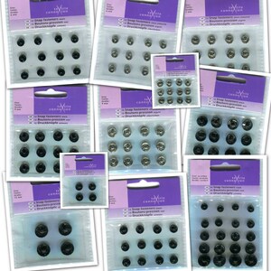 May include: A close-up of 12 packs of black and silver snap fasteners. Each pack contains 12 snap fasteners and is labelled "Textile Connection" with the text "Snap fasteners, Boutons-pression, Druckknöpfe".