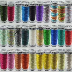 May include: A collection of 18 spools of metallic thread in various colours, including green, red, blue, gold, silver, and white. Each spool is labelled with the brand name "Gütermann" and "Sulky" and a product number.