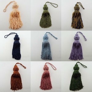 May include: Nine different colours of tassel trim with a loop for hanging. The tassels are made of a soft, fluffy material and are available in a variety of colours, including beige, green, blue, purple, brown, pink, and dark green.