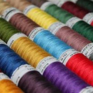 May include: A collection of spools of thread in various colours, including red, blue, green, yellow, and purple. The spools are arranged in a row, with the labels facing the viewer. The labels include the thread colour and the brand name.
