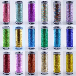May include: Twelve spools of metallic thread in various colours, including pink, blue, purple, green, gold, and silver. Each spool is labelled with the brand name "Sulky" or "Gütermann" and a product number.