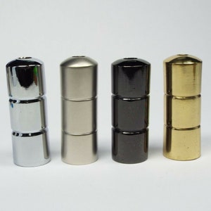 May include: Four metal finials in different finishes: chrome, nickel, black, and brass. Each finial has a cylindrical shape with a slightly rounded top and a grooved design.