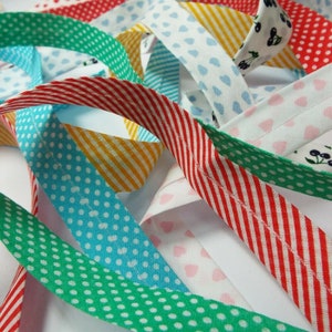 May include: Close-up of colourful bias tape in various patterns. The tape features stripes, polka dots, and heart prints in red, green, blue, yellow, and white. The bias tape is likely used for sewing and crafting projects.
