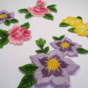 May include: Five embroidered flower appliques in various colours, including pink, purple, and yellow. The appliques are perfect for adding a touch of floral charm to clothing, bags, or home decor projects.