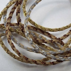 May include: A close-up of a beige cord with gold and silver metallic threads woven into the cord.