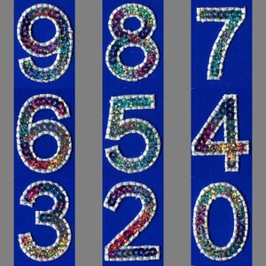 May include: Nine colourful, sparkly, sequined numbers, 9, 8, 7, 6, 5, 4, 3, 2, and 0, on a blue background.