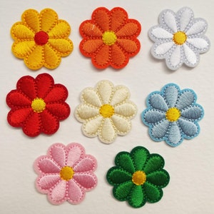 May include: Assortment of eight embroidered iron-on patches featuring daisy flowers in various colours, including yellow, orange, red, white, cream, light blue, pink, and green.