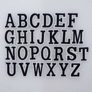 May include: A set of 26 white felt iron-on letters in black, representing the English alphabet, A through Z.