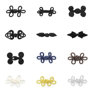 May include: A selection of decorative frog closures in various colours, including black, navy blue, brown, gold, and white. The closures feature intricate knotted designs, suitable for clothing or craft projects. The closures are displayed on a white background.