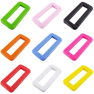 May include: Assortment of ten plastic slider buckles in various colours, including green, pink, black, orange, blue, magenta, red, white, and yellow. Each buckle is rectangular with a rounded edge and a centre opening.