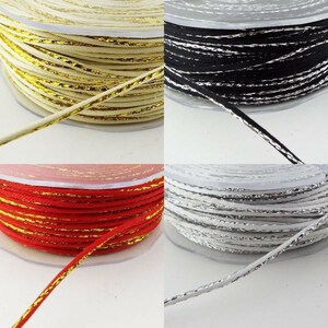 May include: Four spools of cord with a metallic gold thread running through the centre. The cords are cream, black, red, and white.