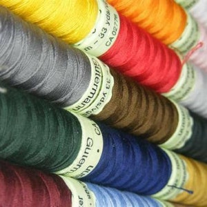 May include: A collection of spools of thread in various colours, including yellow, red, grey, green, brown, blue, and pink. The spools are labelled with the brand name "Gütermann" and the yardage.