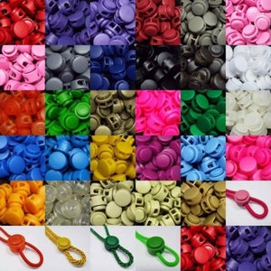 May include: Assortment of plastic toggle cord locks in various colours, including red, blue, green, yellow, purple, pink, black, white, grey, and brown. The toggles are shown in bulk and individually on cords.