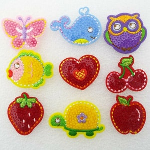May include: A selection of embroidered patches in various shapes and colours. Designs include a pink butterfly, blue whale, purple owl, yellow fish, red heart, cherries, strawberry, turtle, and apple. Each patch is decorated with sequins and detailed stitching.