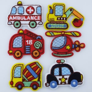 May include: Six embroidered iron-on patches featuring different vehicles: an ambulance, a construction vehicle, a fire engine, a helicopter, a cement mixer, and a police car.