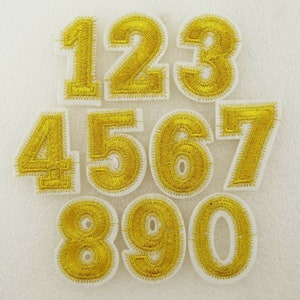 May include: Ten gold iron-on patches featuring the numbers 1 to 10. The numbers are outlined in white and have a shiny gold finish.