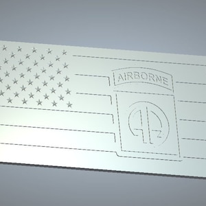 Puede incluir: Un letrero de madera blanco con una bandera estadounidense tallada y las palabras "AIRBORNE" y "101" en un círculo.