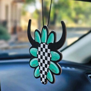 May include: A black and white checkered skull with turquoise flower accents hanging from a rearview mirror. The skull is a car air freshener.