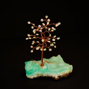 May include: A copper wire tree sculpture with iridescent opal stones for leaves, set on a green and white agate base.