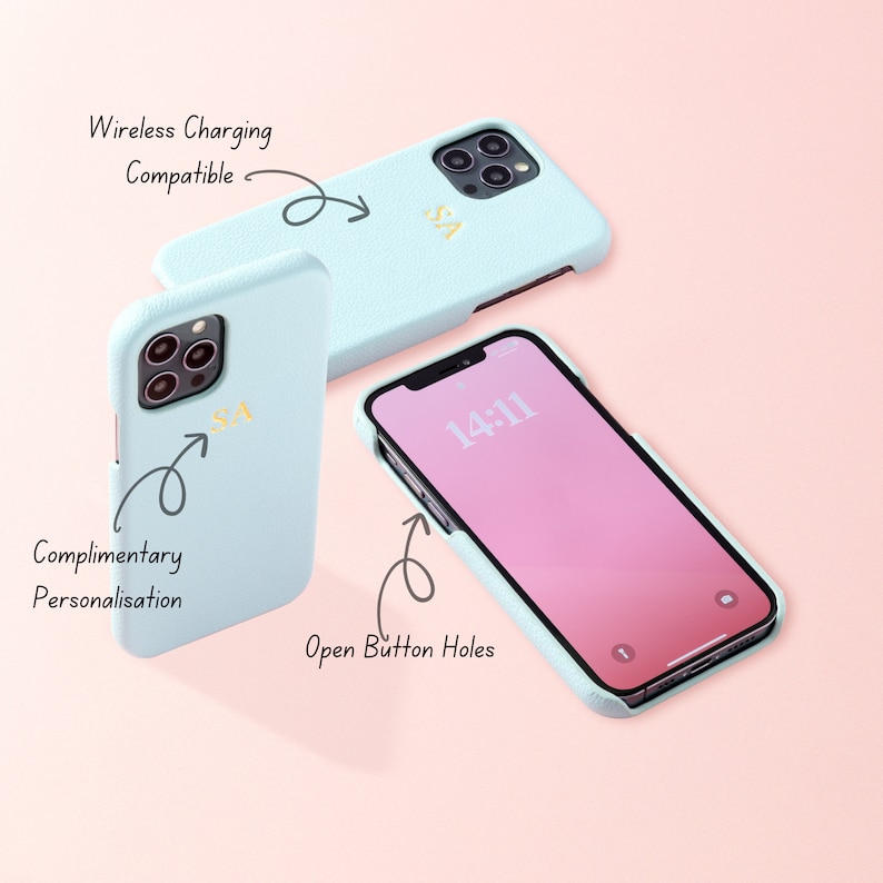 May include: A light blue phone case with a gold monogram "SA" and the text "Wireless Charging Compatible" and "Complimentary Personalisation". The case is shown on a pink background with a phone inside the case. The phone screen shows the time "14:11". The text "Open Button Holes" is written next to the phone.