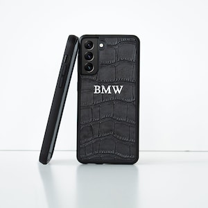 Può includere: Custodia per telefono nera con motivo a coccodrillo e le lettere "BMW" in bianco.