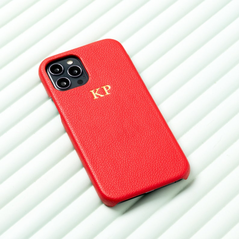 May include: A red leather phone case with a gold monogram "KP" on the back.