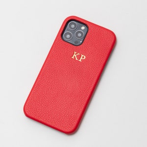 May include: Red leather phone case with a gold monogram "KP" and a black camera lens cutout.
