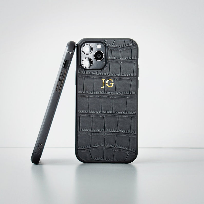 May include: Black phone case with a crocodile pattern and gold initials "JG".