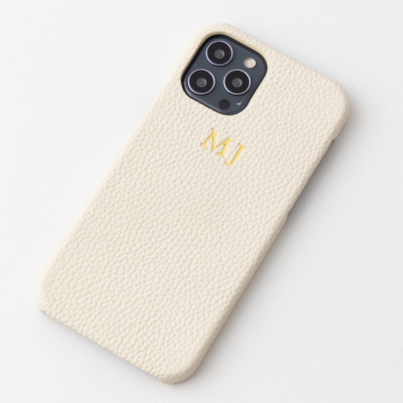 May include: A white leather phone case with a gold monogram "MJ" and a black camera lens cutout.