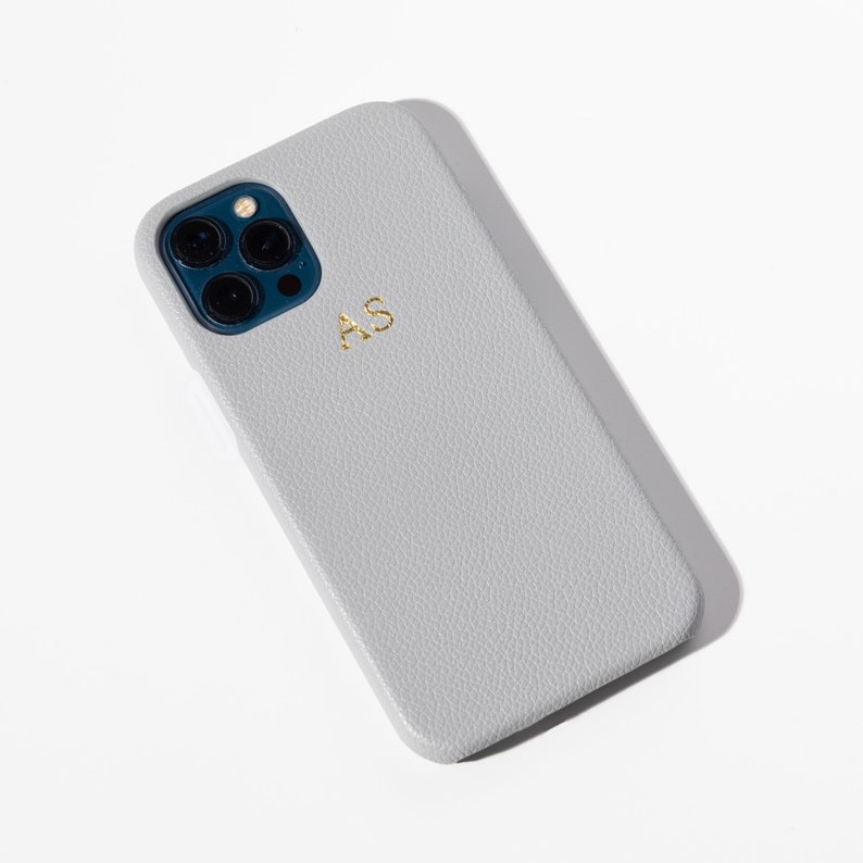 May include: A gray leather phone case with a textured surface and the initials "AS" embossed in gold.